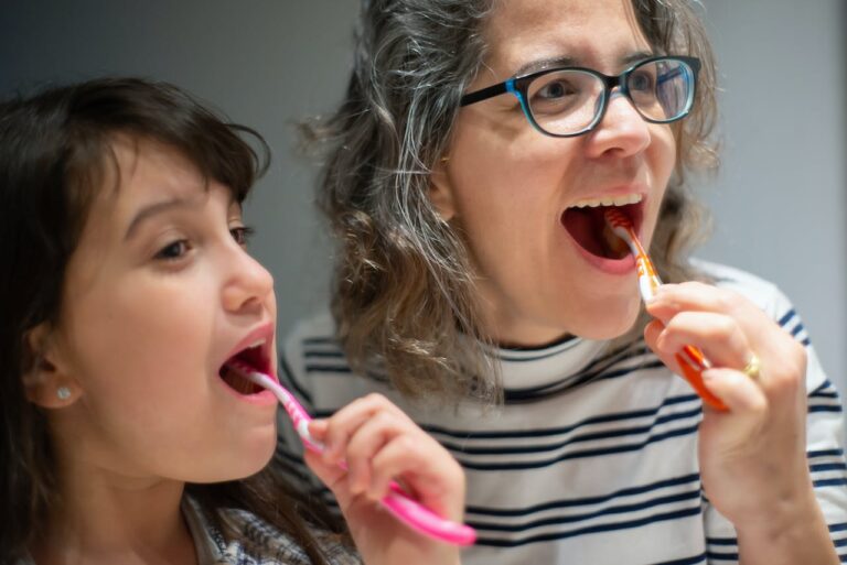 A parent and child brushing their teeth together.