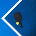A pickleball paddle and ball on the court ready to be used