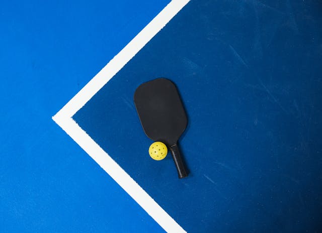 A pickleball paddle and ball on the court ready to be used