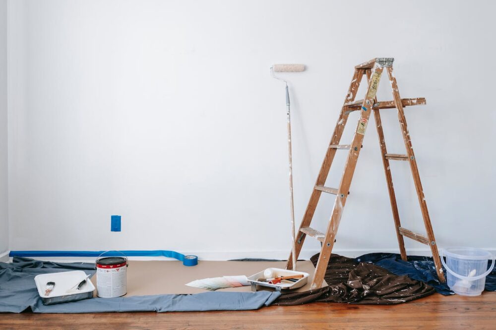 A stepladder, a paint roller, and various painting supplies staged against a wall
