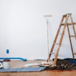 A stepladder, a paint roller, and various painting supplies staged against a wall