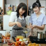 laughing asian mother and daughter preparing pasta in kitchen