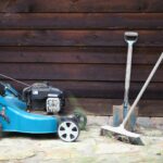 A lawn mower, a broom, and a shovel set against a shed.