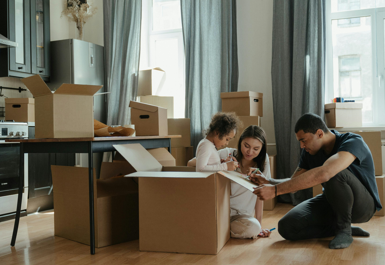 A family of three packing items at home and labeling boxes