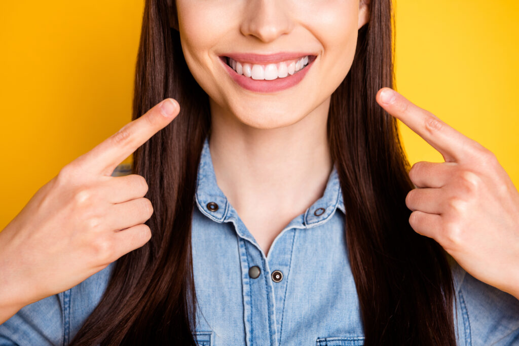 Cropped close up photo of positive girl point index finger teeth demonstrate her perfect white teeth dentist care wear denim jeans shirt isolated over vivid color background