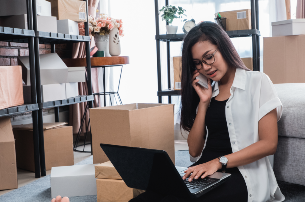 Lady busy with her phone and laptop while packing her items.
