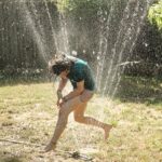 A teenager running through a sprinkler hose spraying water.