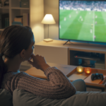 A lady watching football on TV alone at home.