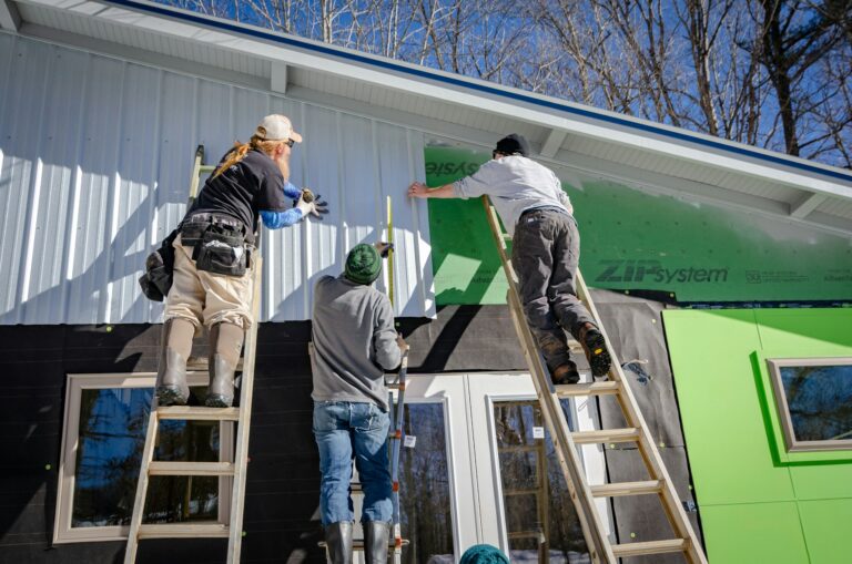 3 workers applying siding to a building nearing completion in the construction process.