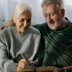 An elderly couple on a couch looking at a book together.