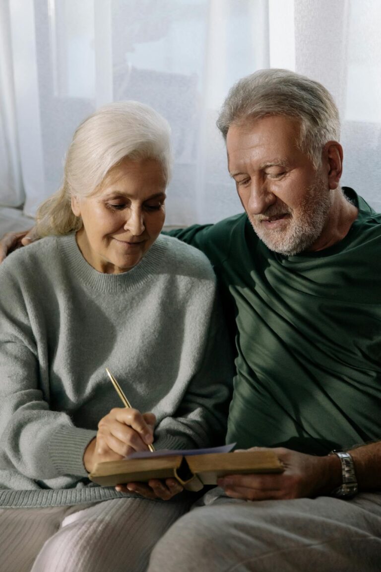 An elderly couple on a couch looking at a book together.