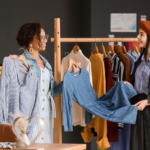 A stylist showing pieces of clothing to her client from a wooden rack.