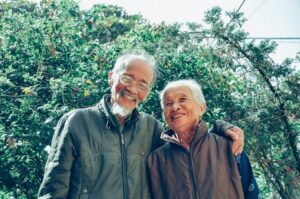 An elderly man with his hand around the shoulder of an elderly woman.