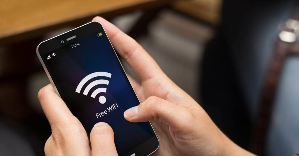 An individual is holding a smartphone in both hands. The screen has an internet symbol and says "Free WiFi."