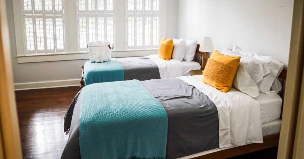 Simple Ways To Impress Short-Term Rental Guests 1 A pair of beds in a clean bedroom. Both beds have neatly arranged and colorful bedding, and one has a basket of towels on it.