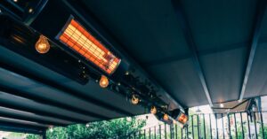 A glowing orange infrared heater on the ceiling of a terrace. There are ivy vines along the same support beam.