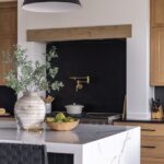 A modern kitchen with wooden cabinets, an island with a waterfall edge, large pendant lights, and a gas range.