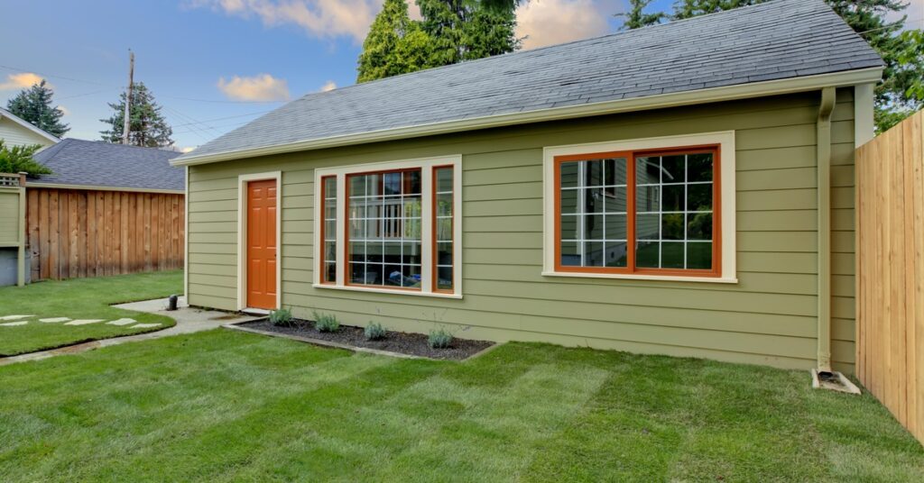 A green detached unit with orange trim and matching door sitting behind a fence, topped with a black asphalt roof.