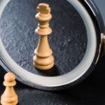 A wooden chess pawn placed in front of a small circular mirror that is reflecting back a chess king.