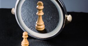 A wooden chess pawn placed in front of a small circular mirror that is reflecting back a chess king.