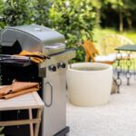 A backyard patio area with a grill and a dining table with chairs. The grass is green and the sun is shining.