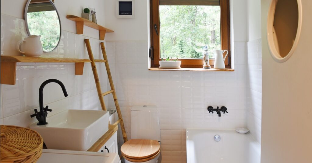 A small rustic bathroom with a white sink, black fixtures, wood accents, a ladder towel rack, and a window view of green trees.