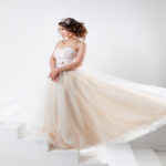 A young woman in a strapless gown with a flowing skirt, standing against a white background with geometric shapes.