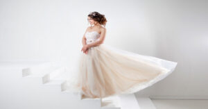 A young woman in a strapless gown with a flowing skirt, standing against a white background with geometric shapes.