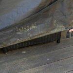 A close-up of a man's hand and foot as he pulls down the cover for outdoor patio furniture on a deck.