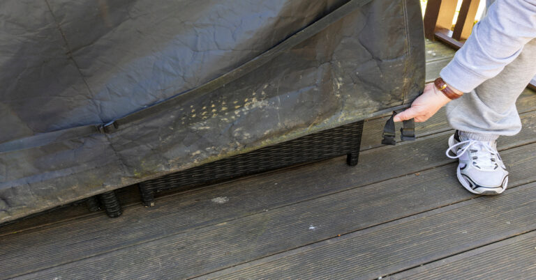 A close-up of a man's hand and foot as he pulls down the cover for outdoor patio furniture on a deck.