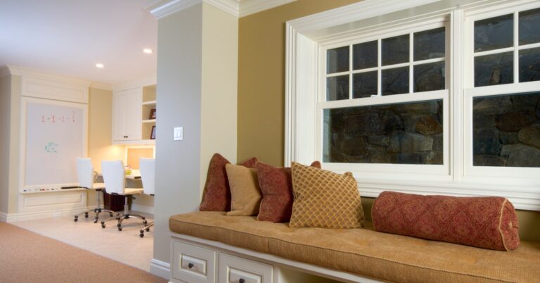 A finished basement in a modern home with a custom-built bench near a window and a home office with a whiteboard.