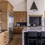 A modern kitchen with wooden cabinets, black hardware, an island with black stools, and cone-shaped light fixtures.