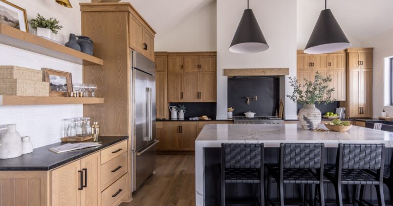 A modern kitchen with wooden cabinets, black hardware, an island with black stools, and cone-shaped light fixtures.