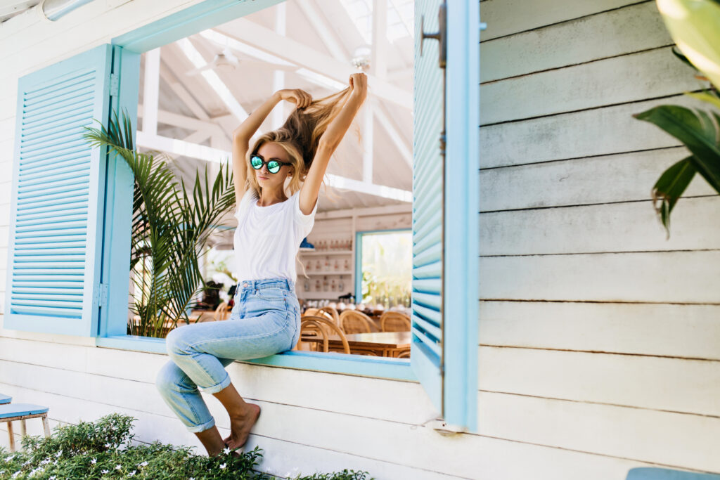 Tanned barefooted woman in vintage jeans playing with her beautiful long hair. Photo of fashionable