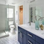 A modern bathroom with a glass walk-in shower, patterned tile floor, and a double sink vanity with blue cabinets.