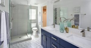 A modern bathroom with a glass walk-in shower, patterned tile floor, and a double sink vanity with blue cabinets.