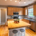 Modern kitchen with warm wooden cabinets, white countertops, and stainless steel appliances