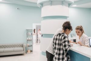 Couple reviewing documents at a medical center reception desk while staff assist.