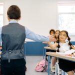Girl gives a classmate a high five in a classroom while other students sit nearby