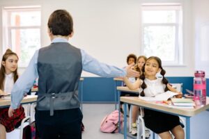 Girl gives a classmate a high five in a classroom while other students sit nearby