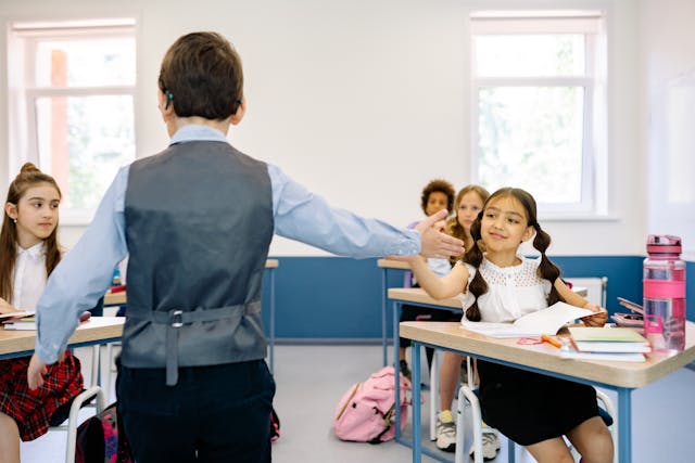 Girl gives a classmate a high five in a classroom while other students sit nearby