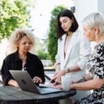 Group of women entrepreneurs meeting outdoors at a café, collaborating around a laptop.