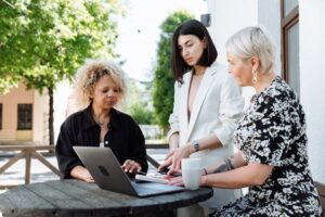 Group of women entrepreneurs meeting outdoors at a café, collaborating around a laptop.