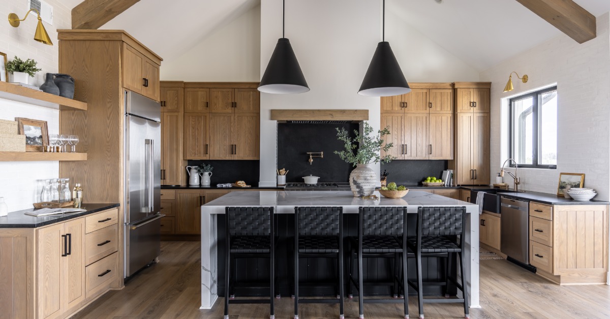 Luxury kitchen with wood cabinetry, a large marble island, black barstools, pendant lights, and exposed beams.